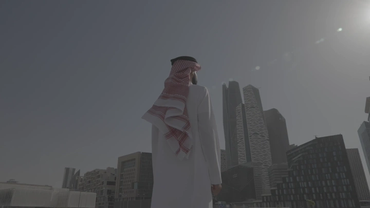 رجل يرتدي ثوبًا ينظر إلى أبراج الرياض، لقطة من الخلف.