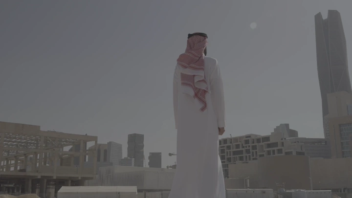 رجل يرتدي ثوبًا ينظر إلى المدينة المالية في الرياض، لقطة نهارية.