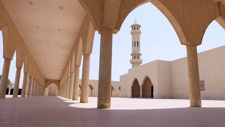 رجل يمشي في ممر مسجد مع مئذنة في وضح النهار، لقطة واسعة.