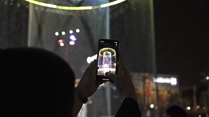 شخص يصور نافورة مضيئة في البوليفارد الرياض ليلاً، لقطة ليلية.