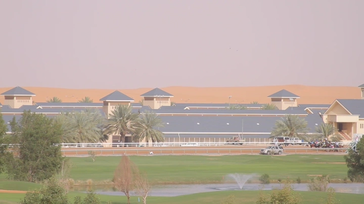 مضمار سباق خيل في الصحراء مع مباني وأشجار، لقطة نهارية.