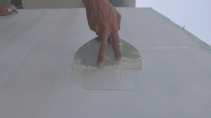 يد تستخدم مجرفة لتسوية الجدار، لقطة قريبة.