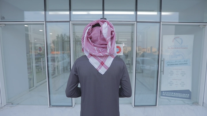 رجل يرتدي شماغًا يدخل مستشفى، لقطة من الخلف.