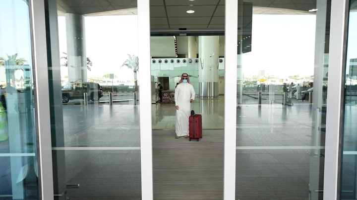 رجل يرتدي الزي التقليدي السعودي يغادر المطار بحقيبة حمراء، لقطة أمامية.