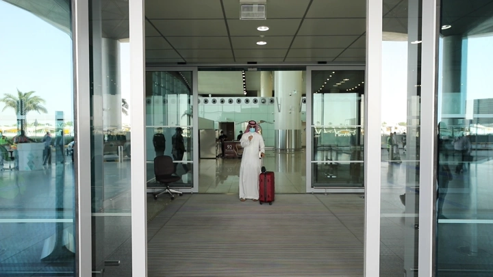 رجل يرتدي ثوبًا يغادر المطار مع حقيبة حمراء، لقطة أمامية.