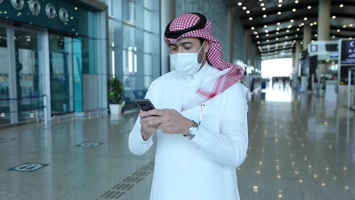 رجل في مطار يستخدم هاتفه لحجز سيارة، لقطة داخلية.