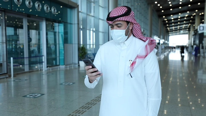 رجل في مطار يستخدم هاتفه لحجز سيارة في المطار، لقطة داخلية.