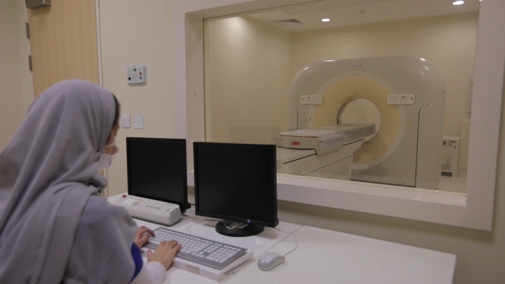 فتاه تجلس أمام شاشات مراقبة جهاز أشعة مقطعية في مستشفى، لقطة داخلية.