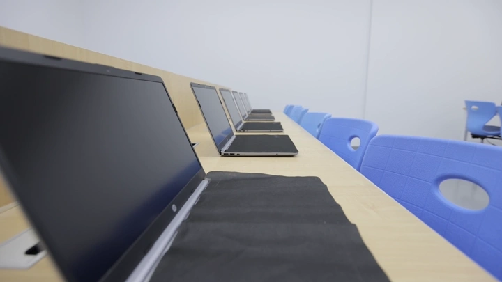 أجهزة لابتوب مرتبة في فصل حاسب آلي بمدرسة، لقطة جانبية.