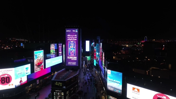 إعلانات مضيئة في البوليفارد بالرياض ليلاً، لقطة جوية.