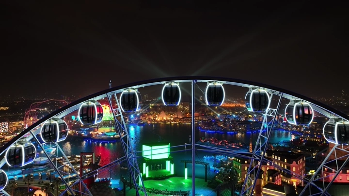 عجلة فيريس مضاءة في بوليفارد وورلد بالرياض ليلاً، لقطة جوية.