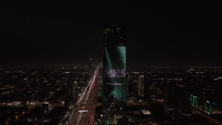 برج في الرياض مضاء بعلم السعودية ليلاً، لقطة جوية.