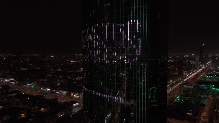 علم السعودية مضاء على برج في الرياض ليلاً، لقطة جوية.