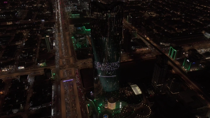 برج في الرياض مضاء بعلم السعودية ليلاً، لقطة جوية.