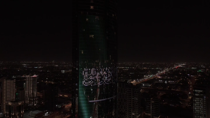 علم السعودية مضاء على برج في الرياض ليلاً، لقطة جوية.