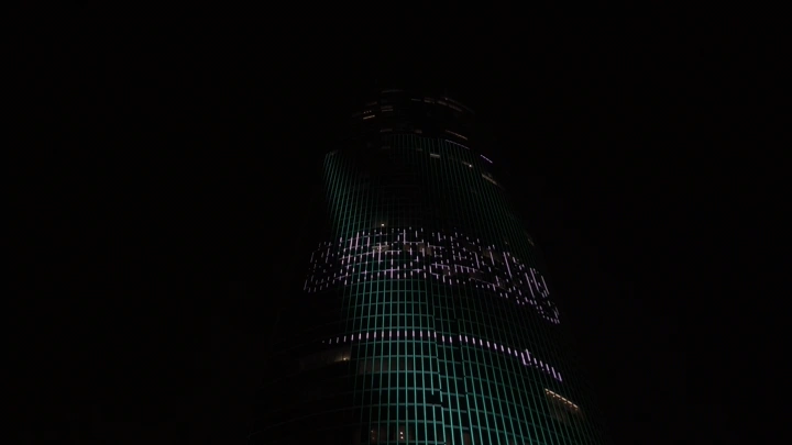 برج مضاء بعلم السعودية في الليل، لقطة من الأسفل.