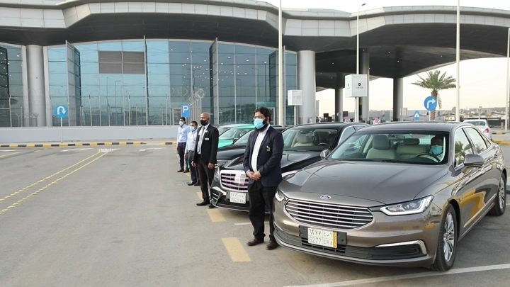 سيارات مصطفة مع موظفين أمام مطار الرياض للتأجير، لقطة نهارية.