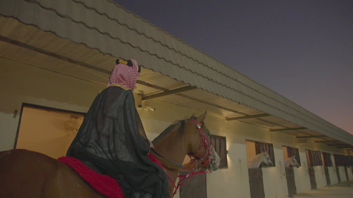 راكب خيل أمام إسطبل عند الغروب، لقطة جانبية.