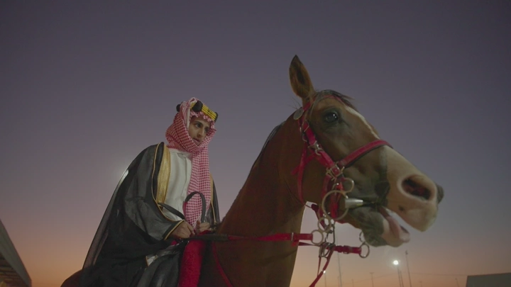 فارس يرتدي الزي السعودي على حصان عند الغروب، لقطة قريبة.