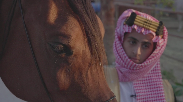 شاب يرتدي الزي السعودي يقف بجانب خيل، لقطة مقربة.
