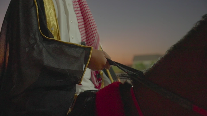 راكب خيل يرتدي الزي السعودي عند الغروب، لقطة قريبة.