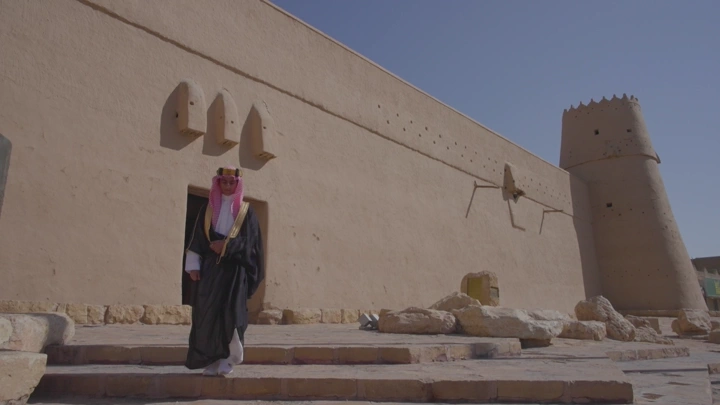 شاب يرتدي الزي السعودي يخرج من قصر المصمك في الرياض، لقطة نهارية.