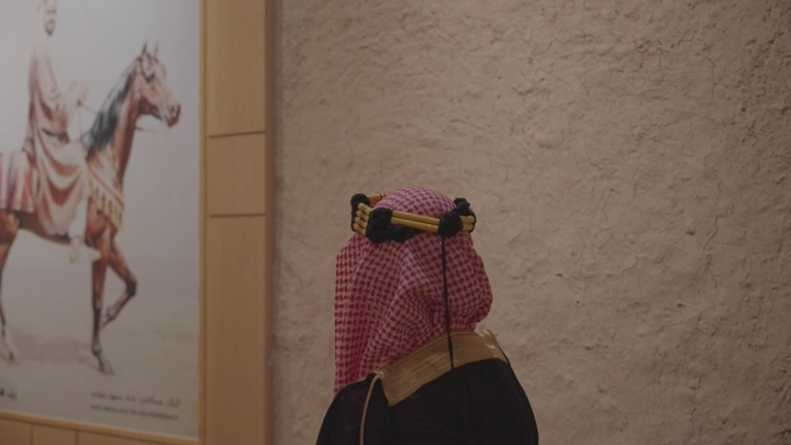 رجل يرتدي الزي السعودي ينظر إلى اللوحات والصور في قصر المصمك بالرياض، لقطة داخلية.