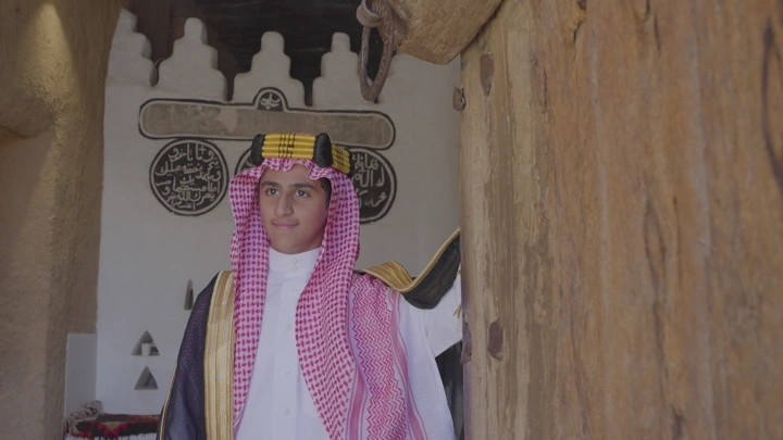 شاب يرتدي الزي السعودي يقف داخل قصر المصمك، لقطة داخلية.