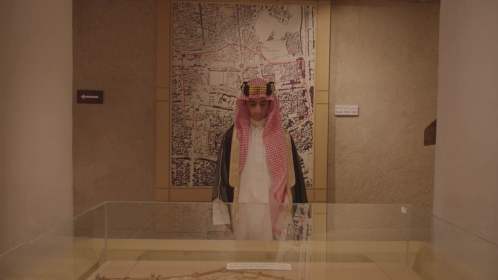 رجل يرتدي الزي السعودي يقف أمام خريطة في قصر المصمك في الرياض، لقطة داخلية.