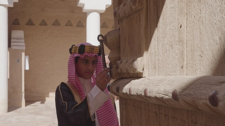 شاب يرتدي الزي السعودي يدق باب في قصر المصمك بالرياض، لقطة قريبة.