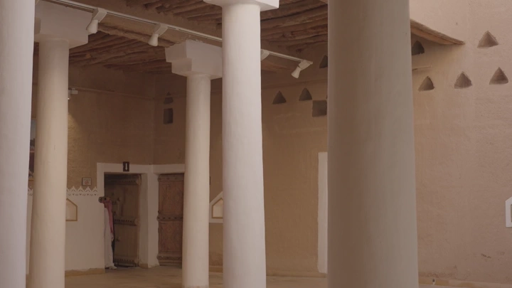 شاب يمشي بين أعمدة داخل قصر المصمك بالرياض، لقطة داخلية.