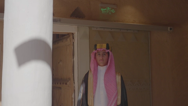 رجل يرتدي الزي السعودي يقف داخل قصر المصمك، لقطة أمامية.