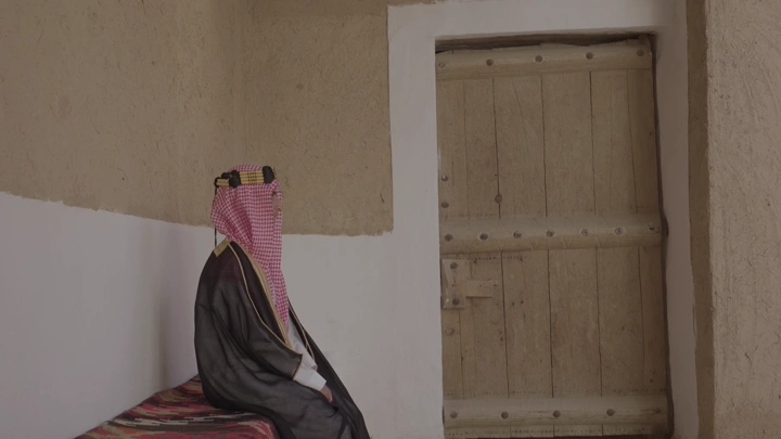 شاب يرتدي الزي السعودي يجلس في قصر المصمك، لقطة داخلية.