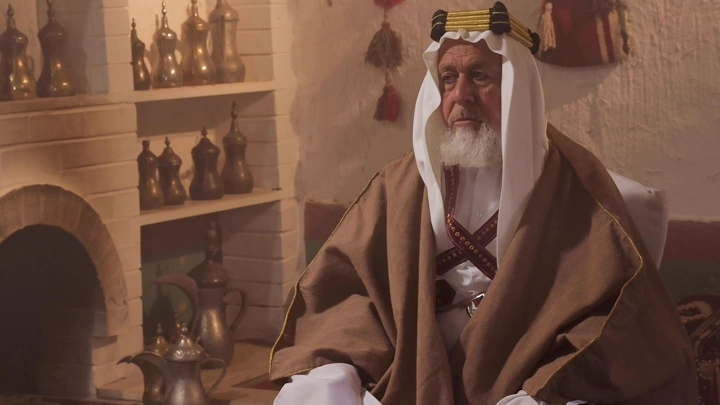 رجل مسن بلباس سعودي تقليدي في غرفة تراثية، لقطة داخلية.