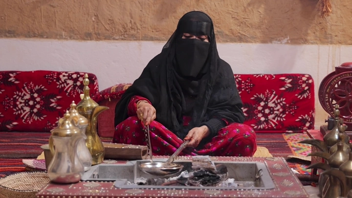 امرأة بلباس تقليدي سعودي تحمس القهوة في مجلس عربي، لقطة داخلية.
