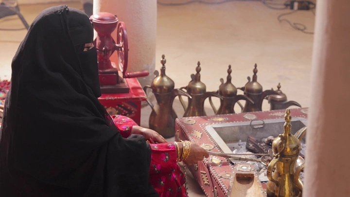 امرأة ترتدي لباس تراثي سعودي تحمس القهوة، تصوير داخلي.