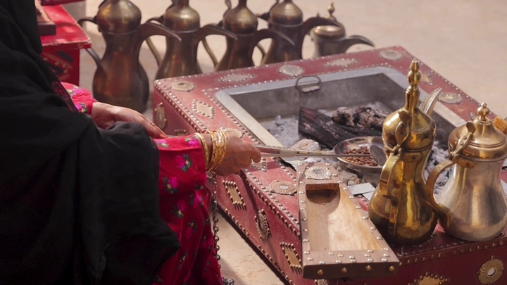 امرأة بلباس تراثي سعودي تحمس القهوة في الهواء الطلق، لقطة قريبة.