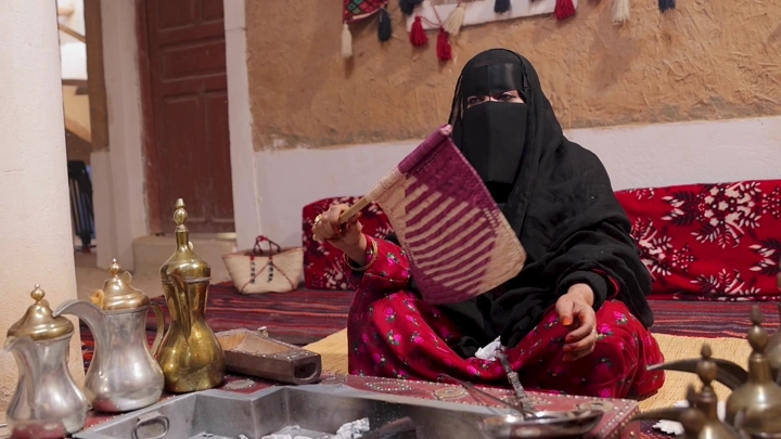 امرأة بلباس تقليدي سعودي تجلس في منزل تراثي، لقطة داخلية.