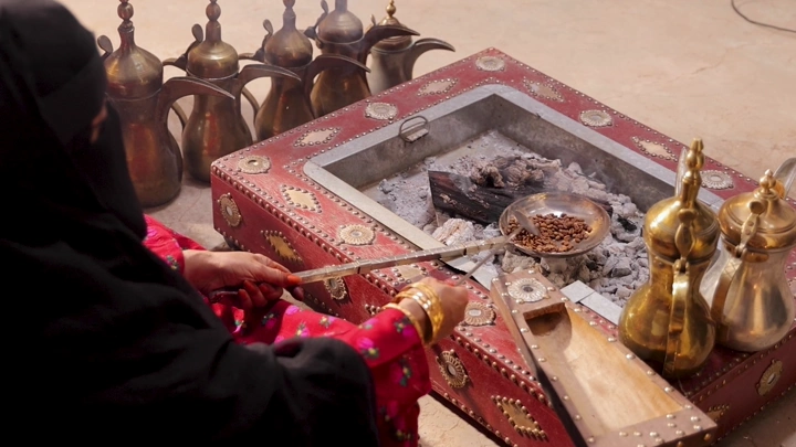 امرأة بلباس تراثي سعودي تحمس القهوة على الحطب، لقطة قريبة.