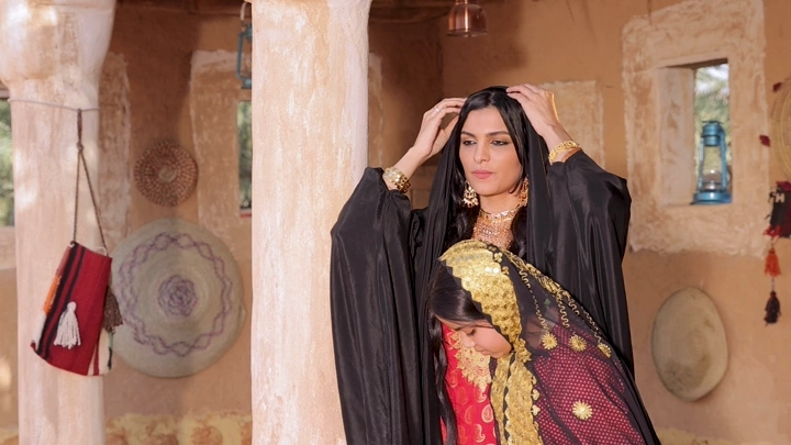 أم وابنتها بلباس تراثي سعودي في بيت طيني، لقطة داخلية.