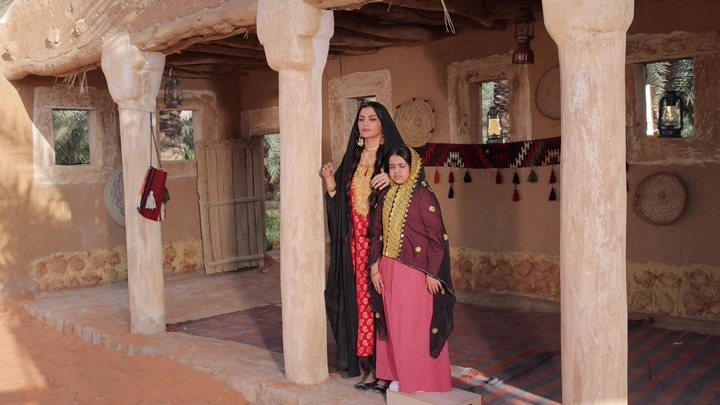 امرأة وفتاة بلباس تراثي سعودي في بيت طيني، لقطة أمامية.