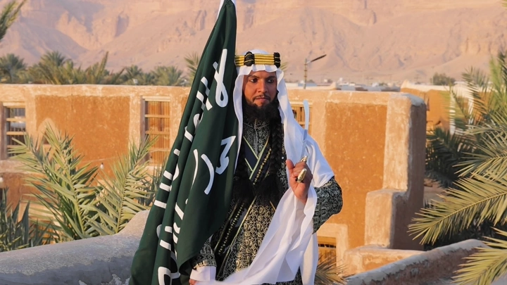 رجل بلباس تراثي سعودي يحمل علم السعودية القديم، لقطة طبيعية.