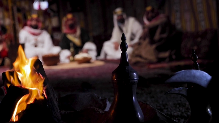 رجال بلباس تقليدي سعودي في خيمة مع دلال قهوة، لقطة داخلية.