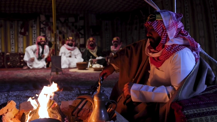 رجال بلباس تراثي سعودي في خيمة بجانب الحطب، لقطة ليلية.