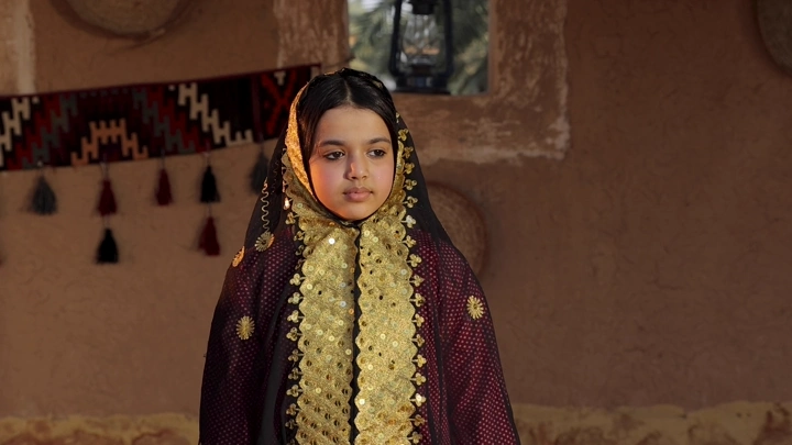 فتاة ترتدي زيًا تراثيًا سعوديًا في منزل تقليدي، لقطة داخلية.