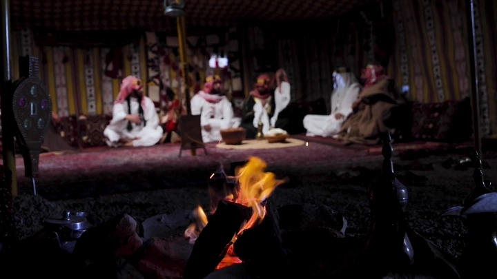مجموعة رجال بلباس تقليدي سعودي في خيمة، لقطة ليلية.