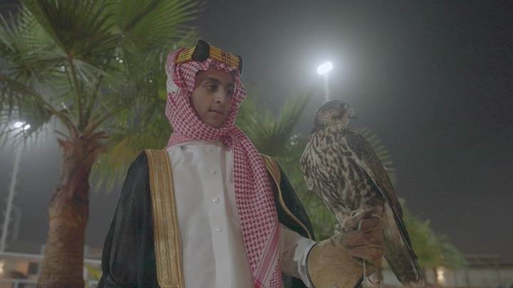 شاب يرتدي الزي السعودي يحمل صقر في الليل، لقطة قريبة.