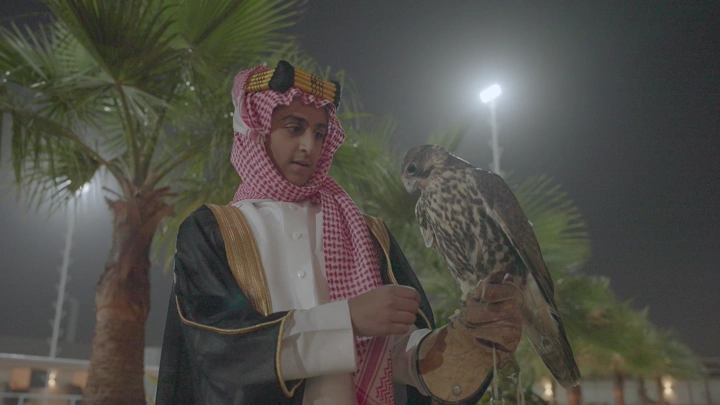 شاب يرتدي الزي السعودي يحمل صقر في الليل، لقطة قريبة.