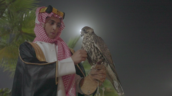 شاب يرتدي الزي السعودي يحمل صقر في الليل، لقطة قريبة.
