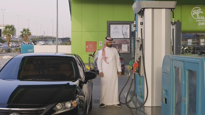 رجل يرتدي الثوب ويعبئ البانزين في محطة وقود، لقطة نهارية.